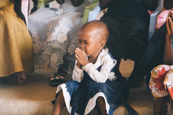 Betendes Kind bei afrikanischer Festlichkeit. In Sierra Leone spielt die Religion eine wichtige Rolle. Erfahre mehr dazu im Beitrag!