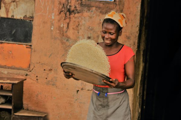 Blick auf eine afrikanische Frau, die Reis in einer großen Schüssel vor sich schwenkt. Erfahre mehr über das Essen in Sierra Leone!